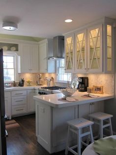 a kitchen with white cabinets and stools next to an island in front of a window