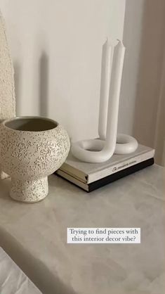 a white vase sitting on top of a table next to a book and candle holder