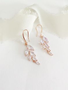 two pairs of gold earrings with white crystals on top of each earring, sitting on a white cloth