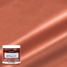 a jar of metallic paint sitting on top of a brown table next to a red wall