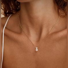 a woman wearing a necklace with a white pearl on it's side and a gold chain