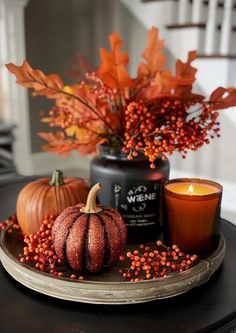 a table topped with candles and pumpkins next to a vase filled with leaves on top of a plate