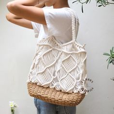 a woman is holding a straw bag in front of her face while standing next to a plant