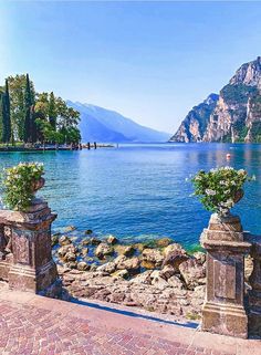 a lake with mountains in the background and some plants on it's sides, surrounded by stone pillars