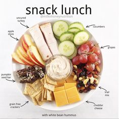 a plate with crackers, cucumbers, apples, grapes and cheese on it