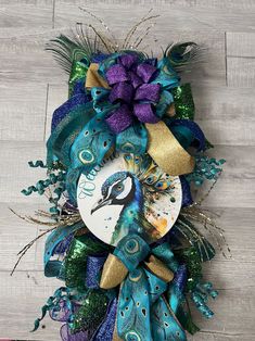 a peacock wreath with purple flowers and green feathers on a wooden floor in front of a white wall