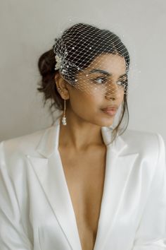 a woman wearing a white suit with a birdcage veil on her head and earrings