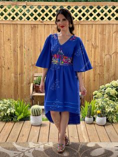 a woman in a blue dress is standing on a wooden deck next to some succulents