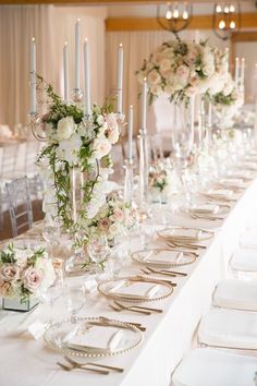 a long table is set with white flowers and silverware for an elegant wedding reception