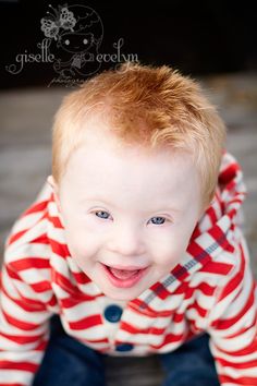 a little boy that is smiling and wearing a red and white striped shirt with his hands in the air