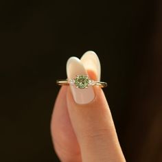 a woman's hand holding an engagement ring with a green stone