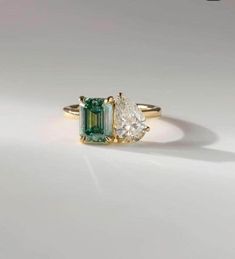 an emerald and diamond three stone ring on a white surface, with the top one in yellow gold