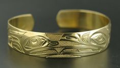 This is a new, hand-engraved, Northwest Coast Native First Nations gold cuff bracelet. Depicting Raven and Frog, this exquisitely carved gold bracelet measures 1/2" x 6" and will fit a wrist between 6 1/4" - 6 3/4" in circumference. It is signed on the inside by Kelvin Thompson and weighs roughly 18 grams solid 14k gold.Raven is often paired with Frog in Native art from the Pacific Northwest because Frog is viewed as the one who communicated Raven's knowledge to the people. These symbols also re Symbolic Formal Jewelry With Etched Details, Formal Symbolic Etched Jewelry, Adjustable Yellow Gold Hallmarked Cuff Bracelet, Luxury Brass Bracelets With Polished Finish, Unique Yellow Gold Cuff Bracelet For Formal Occasions, Carved Symbolic Yellow Gold Jewelry, Yellow Gold Symbolic Carved Jewelry, Symbolic Carved Jewelry For Formal Occasions, Luxury Engraved Cuff Bracelet For Anniversary