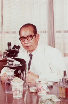 a man sitting at a table in front of a microscope and some cups with sauces on it