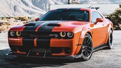 an orange and black car parked in a parking lot with mountains in the back ground