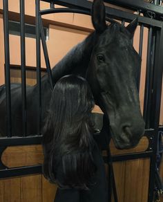 a woman standing next to a black horse in a stable with its head over the gate