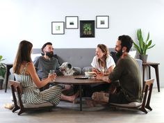 three people sitting at a table talking and drinking wine with a dog in the background