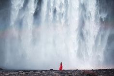 a woman standing in front of a waterfall with a rainbow above her head and water falling off the side