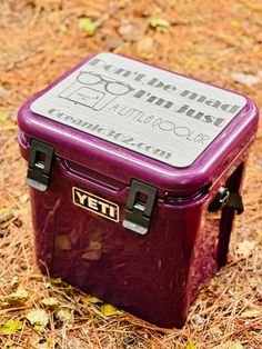 a purple cooler sitting on the ground in front of some dry grass and dead leaves