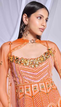 Our burnt orange 3-piece sharara set includes a peplum top, sharara, and dupatta. The peplum top features delicate embroidery with crystals, pearls, and sequins, complemented by gold metallic flowers on the front neckline and scalloped hem. The georgette sharara is adorned with crystal tassels, while the matching dupatta is embellished with scattered embroidery and finished with a delicate pearl and golden border. This ensemble offers a perfect blend of opulence and elegance. Orange Designer Palazzo Set For Navratri, Orange Palazzo Set With Dupatta And Traditional Drape, Semi-stitched Orange Palazzo Set With Gota Work, Traditional Drape Orange Palazzo Set With Dupatta, Designer Orange Palazzo Set With Zari Work, Orange Bollywood Designer Palazzo Set, Semi-stitched Orange Palazzo Set With Zari Work, Orange Palazzo Saree Set For Diwali, Festive Semi-stitched Palazzo Set In Orange