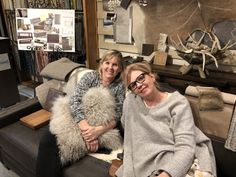 two women are sitting on a couch in a room with many items and decor around them