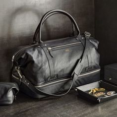 a black leather duffel bag sitting on top of a wooden floor next to a pair of scissors