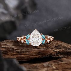 a pear shaped diamond ring with blue and white stones in the center on top of a piece of wood