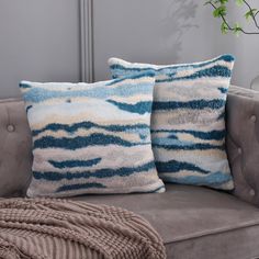 two blue and white pillows sitting on top of a gray couch next to a potted plant