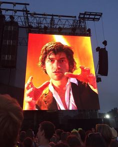 a large screen with a man on it in the middle of a crowd at an outdoor concert