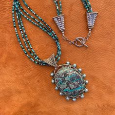 "- A handcrafted, locally sourced, one of a kind, statement necklace. - Chrysocolla is a semi-precious gemstone found in Arizona.  This one was cut and polished by a local rock hound. I bought the cabochon from him at an outdoor Boutique market in our town.  I used silver plated 20 and 26  gauge wire to weave the pendant and bail. I added 13 glass pearls around the edge of the pendant.  I used the same wire plus a small medallion on the back to secure and decorate it.    - The 21\" necklace is m Handmade Malachite Healing Necklace, Artisan Necklace With Amazonite Gemstone Beads, Handmade Amazonite Round Beads Necklaces, Artisan Amazonite Round Bead Necklace, Artisan Necklace With Natural Stones And Amazonite, Artisan Beaded Turquoise Pendant Necklace, Turquoise Malachite Beaded Necklace For Gift, Artisan Turquoise Amazonite Jewelry, Artisan Amazonite Necklace With Natural Stones