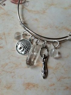 This cute silver-toned metal expandable charm bangle was made with Lammas, or Lughnasadh, in mind. It matches a Lammas themed prayer bead strand I recently made. It would also match most anything else, as well, since the stones used are clear. It's made with a silver-toned metal expandable bangle and features a gemstone point, silver-toned metal charms, and bead dangles. In the center is a small bullet-shaped clear Quartz pendulum point. It has two silver-toned metal charms. One is a Goddess and Spiritual Metal Charm Bracelet With Dangle, Spiritual Charm Bracelet With Dangling Charms, Adjustable Spiritual Charm Bangle Bracelet, Adjustable Spiritual Charm Bangle, Adjustable Spiritual Bangle Charm Bracelet, Spiritual Adjustable Bangle Charm Bracelet, Spiritual Wire Wrapped Crystal Bracelet As Gift, Spiritual Style Wire Wrapped Crystal Bracelet For Gift, Spiritual Nickel-free Charm Bracelet As Gift