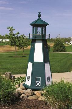 a green and white light house sitting in the middle of a field next to grass