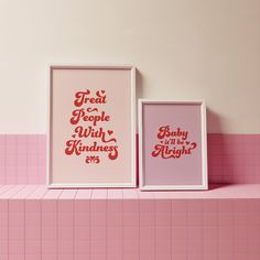 two framed posters sitting on top of a pink shelf