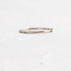 a silver ring sitting on top of a white surface with a small diamond in the middle