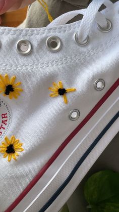 someone is holding a pair of white converse shoes with yellow flowers on the soles