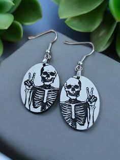 Skeleton making a Peace Sign Earrings - Quirky Halloween Acrylic Jewelry by Fox Tale Laser Add a touch of spooky fun to your accessory collection with our Skeleton Earrings.  Perfect for those who embrace quirky and novelty styles, these earrings are a playful nod to the Halloween season and beyond! Product Features: Design: These earrings feature a charming skeleton making a peace sign, adding a humorous and whimsical twist to your look. Perfect for the Halloween season or for those who love a quirky touch in their everyday wear. Material: Crafted from high-quality two-tone acrylic, these earrings are both lightweight and durable. The white base is elegantly engraved with a striking black skeleton design.  Earring hooks are Stainless Steel Hypoallergenic in silver color. Size: Measuring 1 Peace Sign Earrings, Spooky Earrings, Halloween Acrylic, Black Skeleton, Skeleton Earrings, Skeleton Design, Quirky Earrings, Acrylic Jewelry, Earrings Halloween