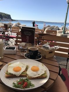 two eggs are on toast with tomatoes and lettuce next to a cup of coffee