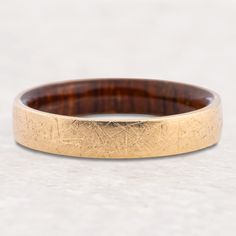 a close up of a gold ring on a white surface with wood in the middle