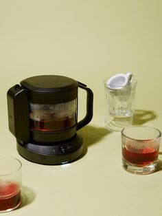 there is a coffee maker and two glasses on the table next to eachother