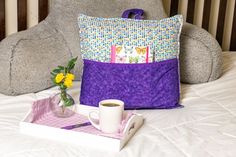 a teddy bear sitting on top of a bed next to a pillow and coffee cup