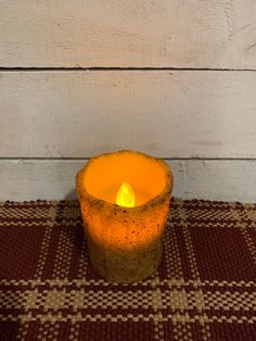 an orange lit candle sitting on top of a brown and white checkered table cloth