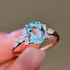 a close up of a person holding a ring with an aqua stone and diamonds on it