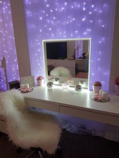 a vanity table with a mirror and lights on the wall next to it in front of a purple curtain