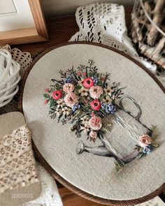 a cross stitch table top with flowers on it and lace doily around the edge