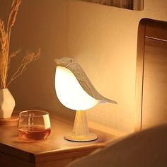 a bird lamp sitting on top of a wooden table next to a wine glass and vase