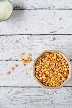 corn kernels in a bowl next to a glass of milk on a white wooden table