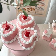 three heart shaped cakes with cherries on top, one is pink and the other is white