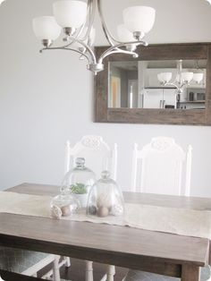 a dining room table with white chairs and a mirror on the wall above it,