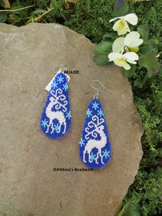 a pair of blue and white beaded earrings sitting on top of a rock next to flowers