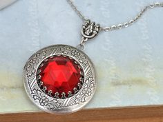 Custom plated antique silver over brass locket with vintage ruby red glass cab mounted on top, locket hangs on 18 inch surgical steel chain with lobster clasp (won't rust or change color). (limited stock) Measurement: Locket is about 1.2 inch (32mm) wide on 18 inch chain. If you have a preferred length for the chain, please let me know in message to seller box and I will adjust it before shipping. Red Locket Necklace With Round Pendant, Red Locket Necklace For Jewelry Making, Red Victorian Engraved Necklace, Victorian Red Engraved Necklace, Red Locket Pendant Jewelry, Red Locket Jewelry With Round Pendant, Red Round Locket Jewelry, Red Medallion Locket Necklace, Red Locket Jewelry